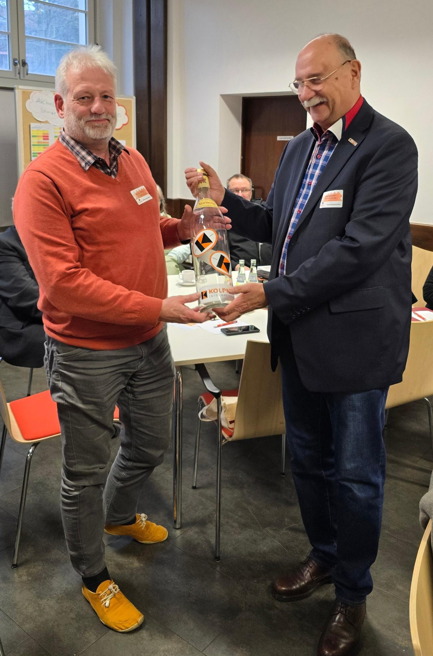 Bernd Münzenhofer übergibt Hans-Bernd Grönewald eine Flasche für Geldspenden.